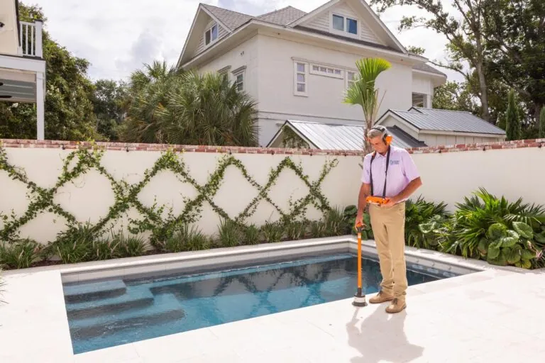Technician checking pool for leaks with equipment near residential swimming pool in sunny backyard garden.