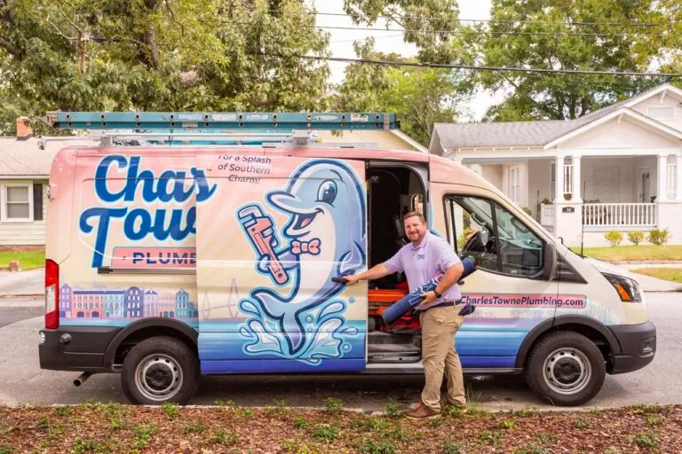 Plumber standing beside a colorful van with a dolphin logo, holding tools in a residential neighborhood.